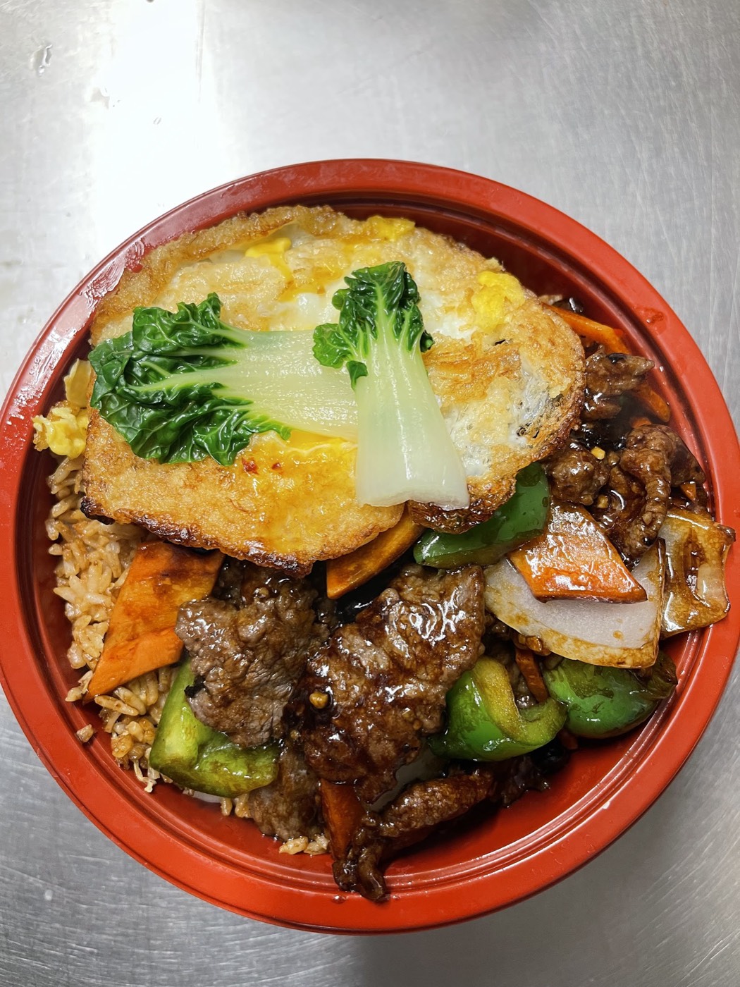Beef in black bean sauce with green pepper over egg fried rice, topped with a fried egg
