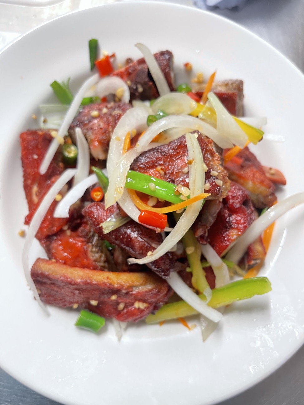 Honey-glazed ribs tossed with onion, spring onion and chilli on a white plate